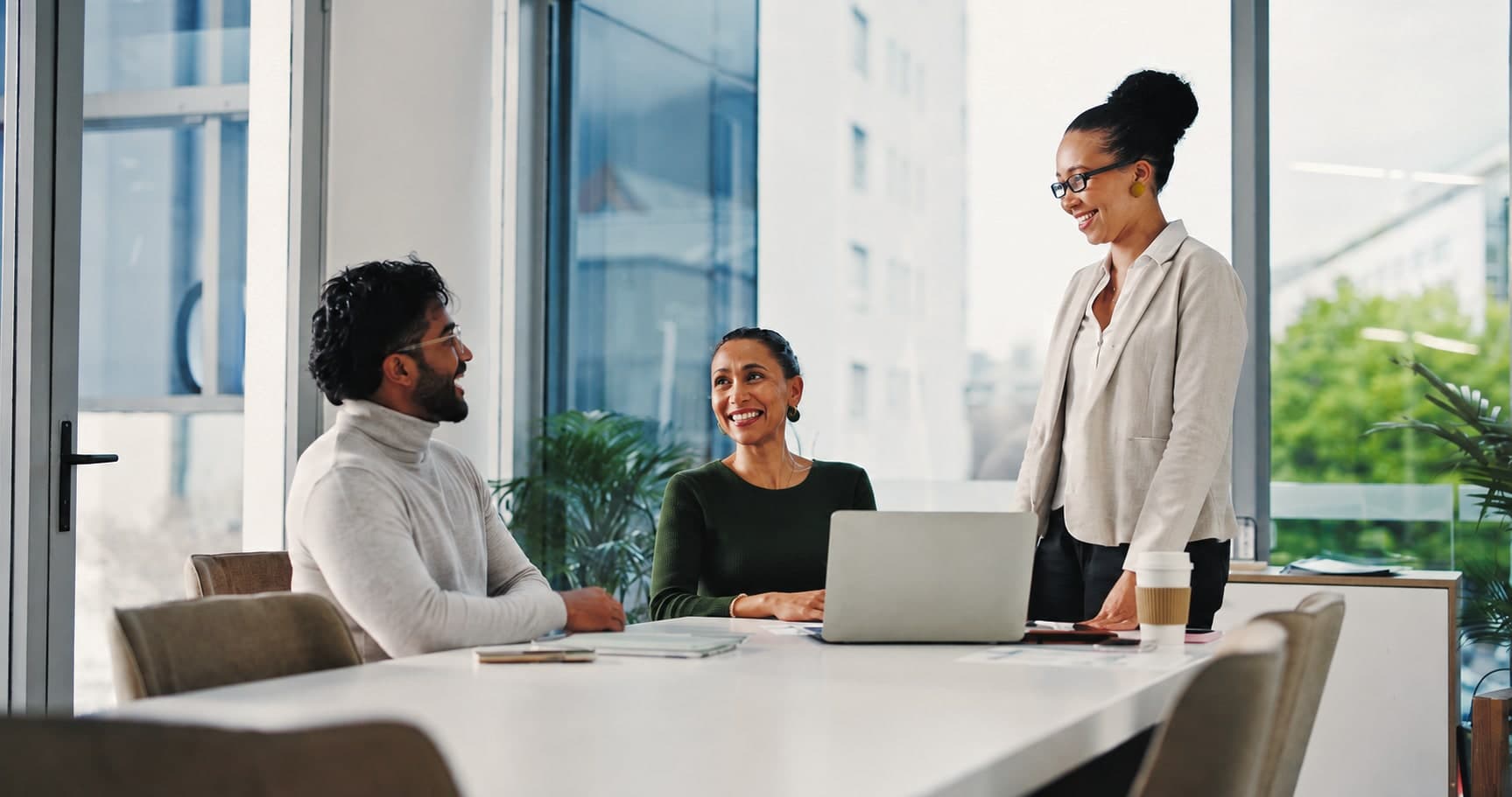 A woman standing at the head of a table, talking with two seated colleagues