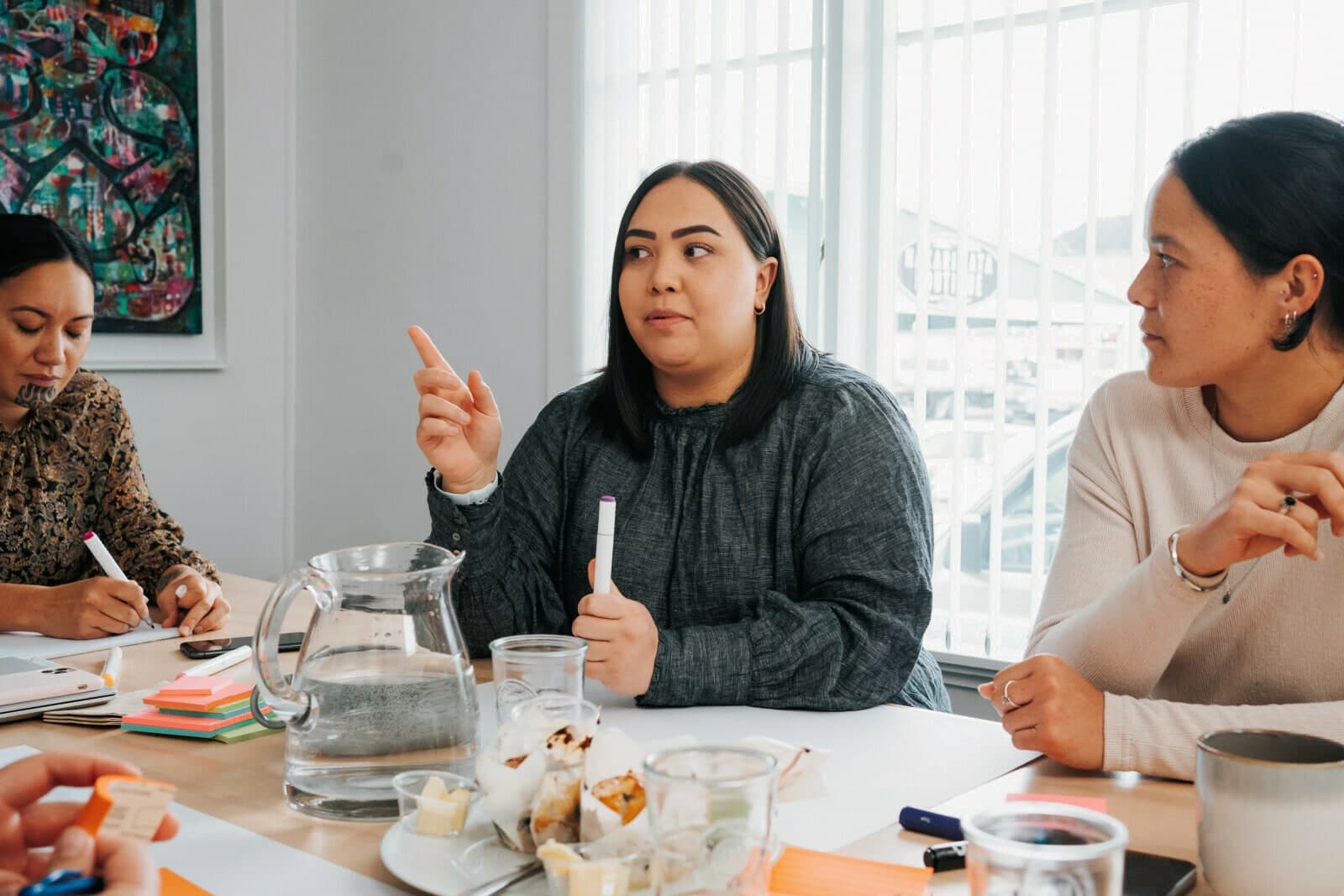 Three women at a workshop table, one gesturing as she speaks
