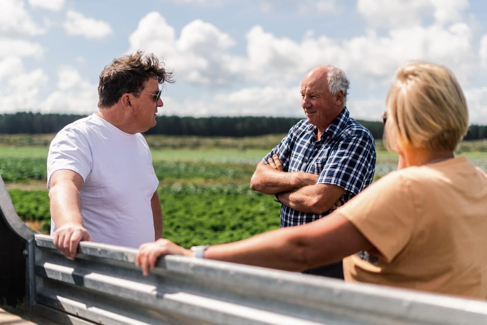 Three people talking at a rail beside a paddock