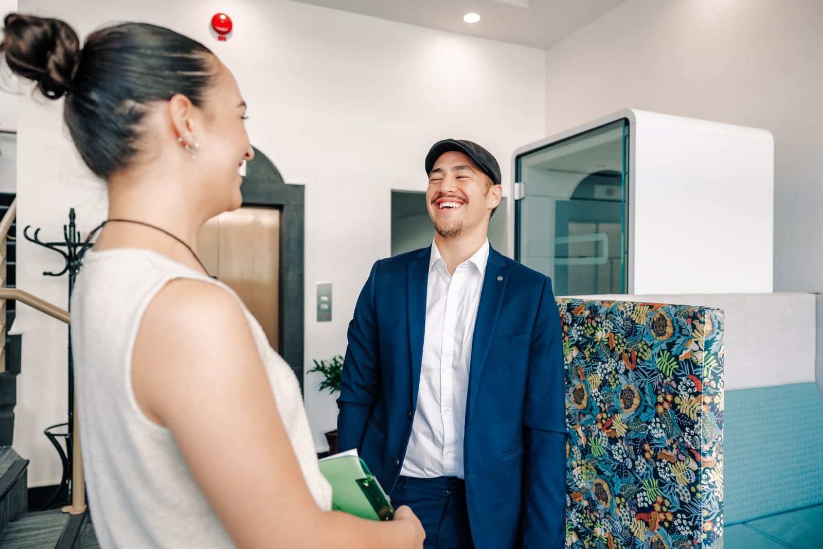 A woman welcoming a smiling man in a navy suit into an office